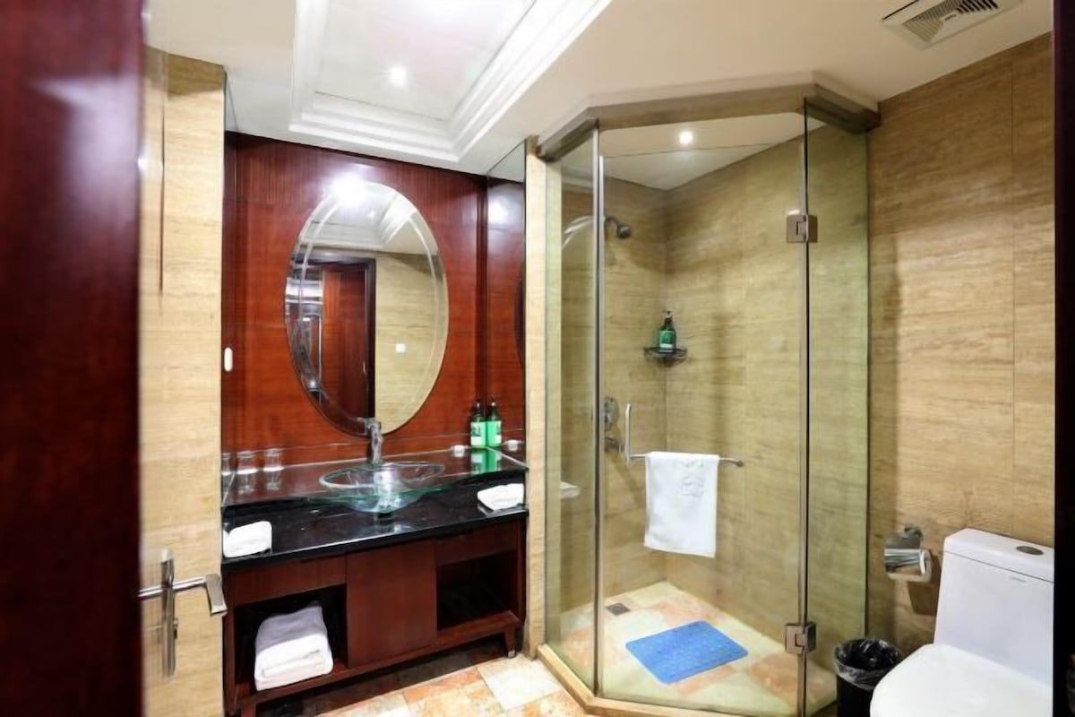 A modern bathroom with a glass-enclosed shower, a wooden vanity with a glass sink, and a large mirror.