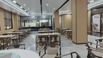 Un comedor amplio con varias mesas y sillas, una zona de cocina central y un ventanal grande a la izquierda.
