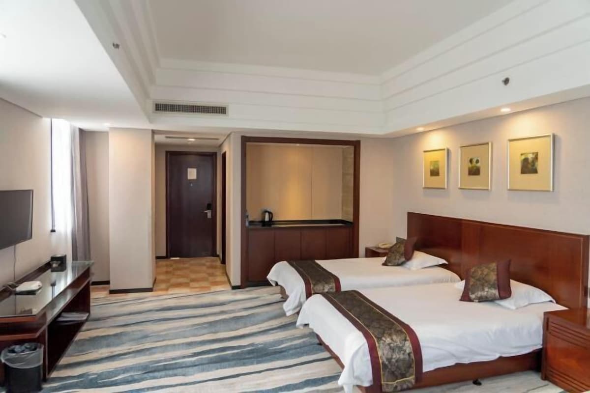 A hotel room with two beds, a TV, a desk, and a bathroom.