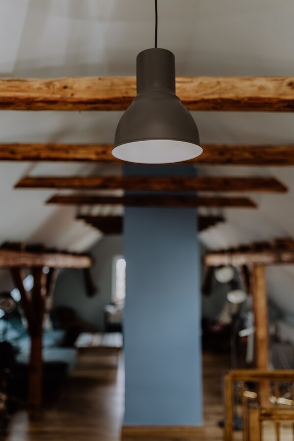 A pendant light hanging from a wooden beam in a room with exposed beams and a blue accent wall. - Lovingly Renovated Farmhouse in Rhön/Kaltenwestheim (Kaltennordheim)