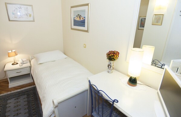A hotel room with a bed, bedside table with a lamp, a small desk with a lamp, a mirror, and a vase with flowers. - Peristil Luxury Rooms (Split)