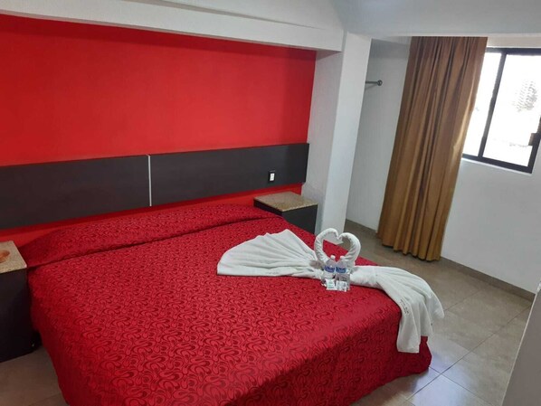 A hotel room with a red bedspread, a white towel, and a bottle of water on the bed. - Hotel Islas Canarias (Tultitlan)