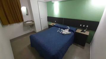 A hotel room with a bed, a bedside table, a nightstand, a mirror, a sink, and a green wall.