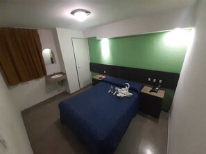 Ett hotellrum med en säng, ett nattduksbord, ett skrivbord, en stol, en spegel, ett fönster och en dörr.