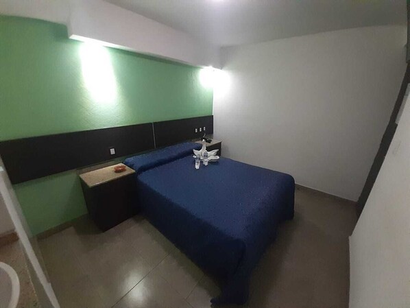 A small, single-bed room with a blue bedspread, a nightstand, a lamp, and a green wall. - Hotel Islas Canarias (Tultitlan)