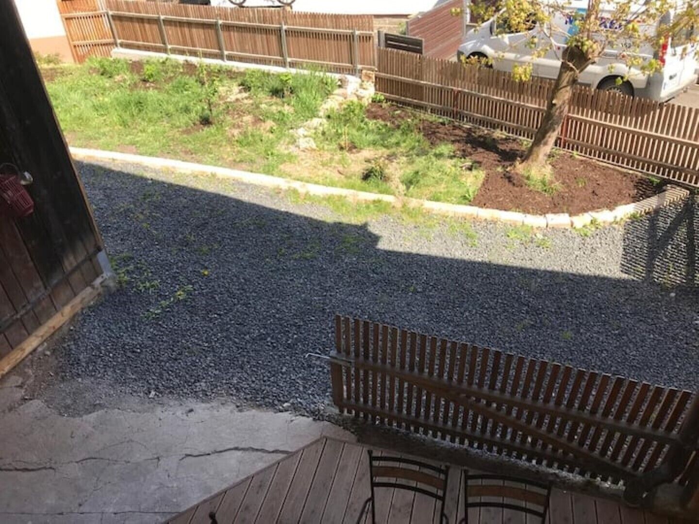 A wooden deck with a bench, gravel pathway, and a fenced garden area.