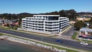 A multi-story hotel with a modern architectural design, located adjacent to a coastal road. - Glorious 2-Bed with Waterside Balcony Views (Batemans Bay)