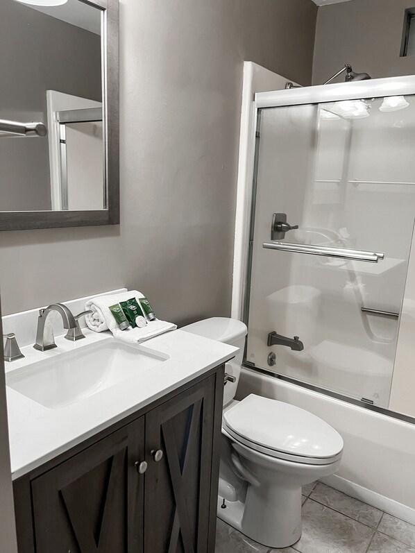 A modern bathroom with a white sink, two faucets, a toilet, and a glass-enclosed shower. - The Southern Charm (Beaufort)