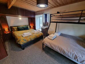 Une chambre avec un lit superposé, un lit simple, une table de chevet avec une lampe et une fenêtre donnant sur l’extérieur.