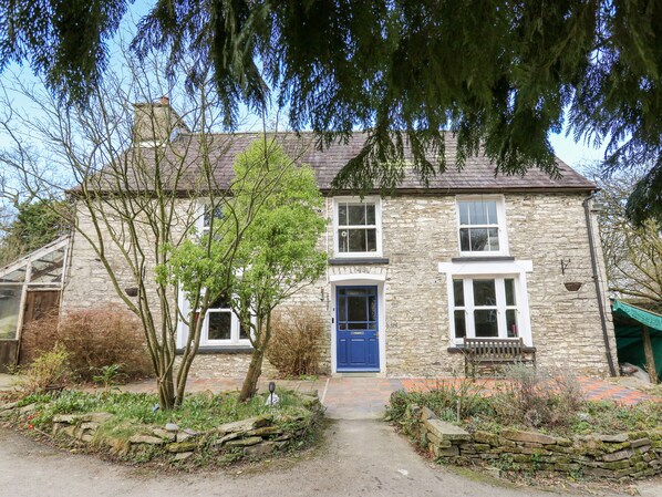 Une maison en pierre avec une porte bleue, un petit jardin et un chemin de pierre menant à l’entrée.
