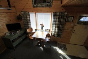 L’intérieur d’une cabane en bois, avec une table à manger, des chaises, une commode verte, un téléviseur et une porte.