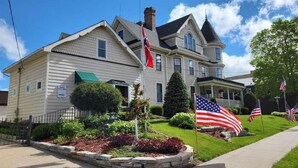A two-story house with a front porch, a flag in front, and a well-maintained lawn. - Westby House Lodge-Scandia Room (Westby)