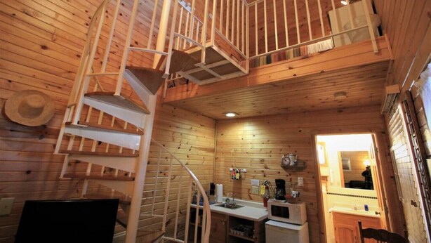 A cabin interior with a spiral staircase, wooden walls, a kitchen area with appliances, and a small dining table. - Westby House Lodge-Scandia Room (Westby)