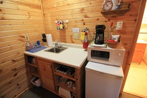 A compact kitchen with wooden paneling, a sink, a microwave, and a coffee maker.