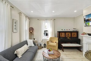 Cozy living room with a comfortable sofa, coffee table, and armchair, featuring a traditional fireplace and a large window.