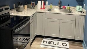 A compact kitchen with white cabinets, a black stove, and a sink. - Cozy Service Station in the heart of Staples (Martindale)