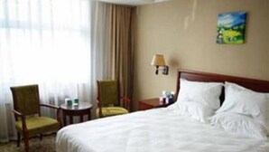 A hotel room with a bed, two chairs, a small table, a lamp, and a painting on the wall. - Greentree Inn Puyang Youtian (Puyang)