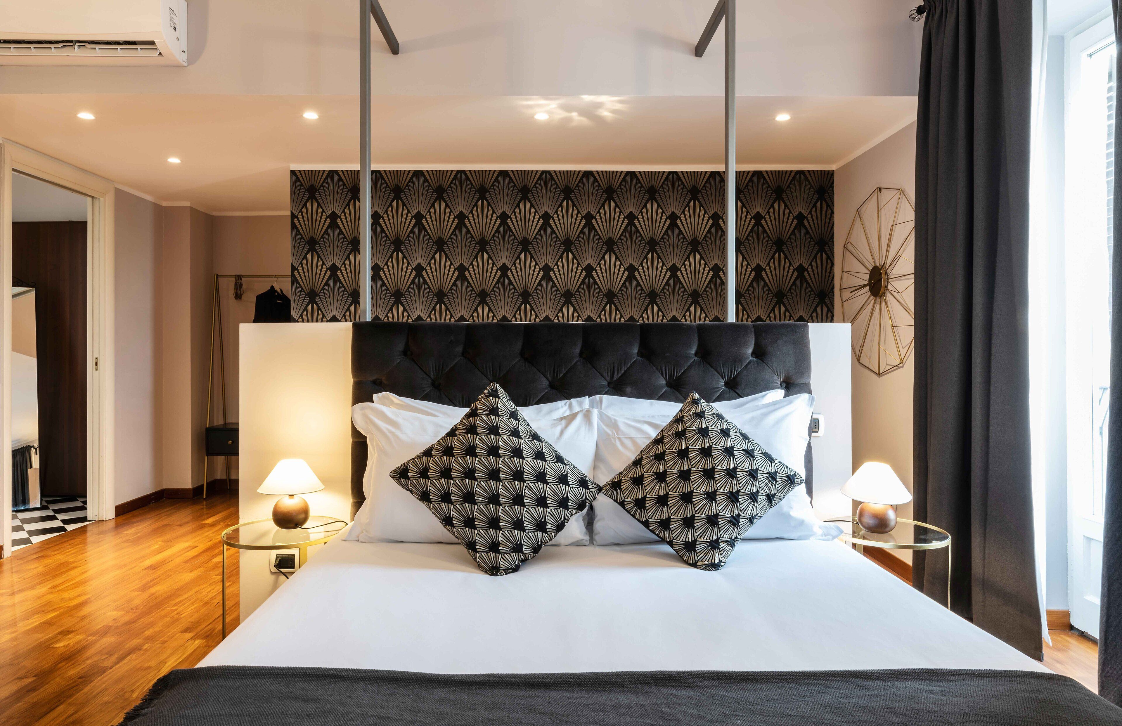Habitación de hotel con una cama grande, dos lámparas de noche, un panel decorativo en la pared y vistas al exterior a través de una ventana.