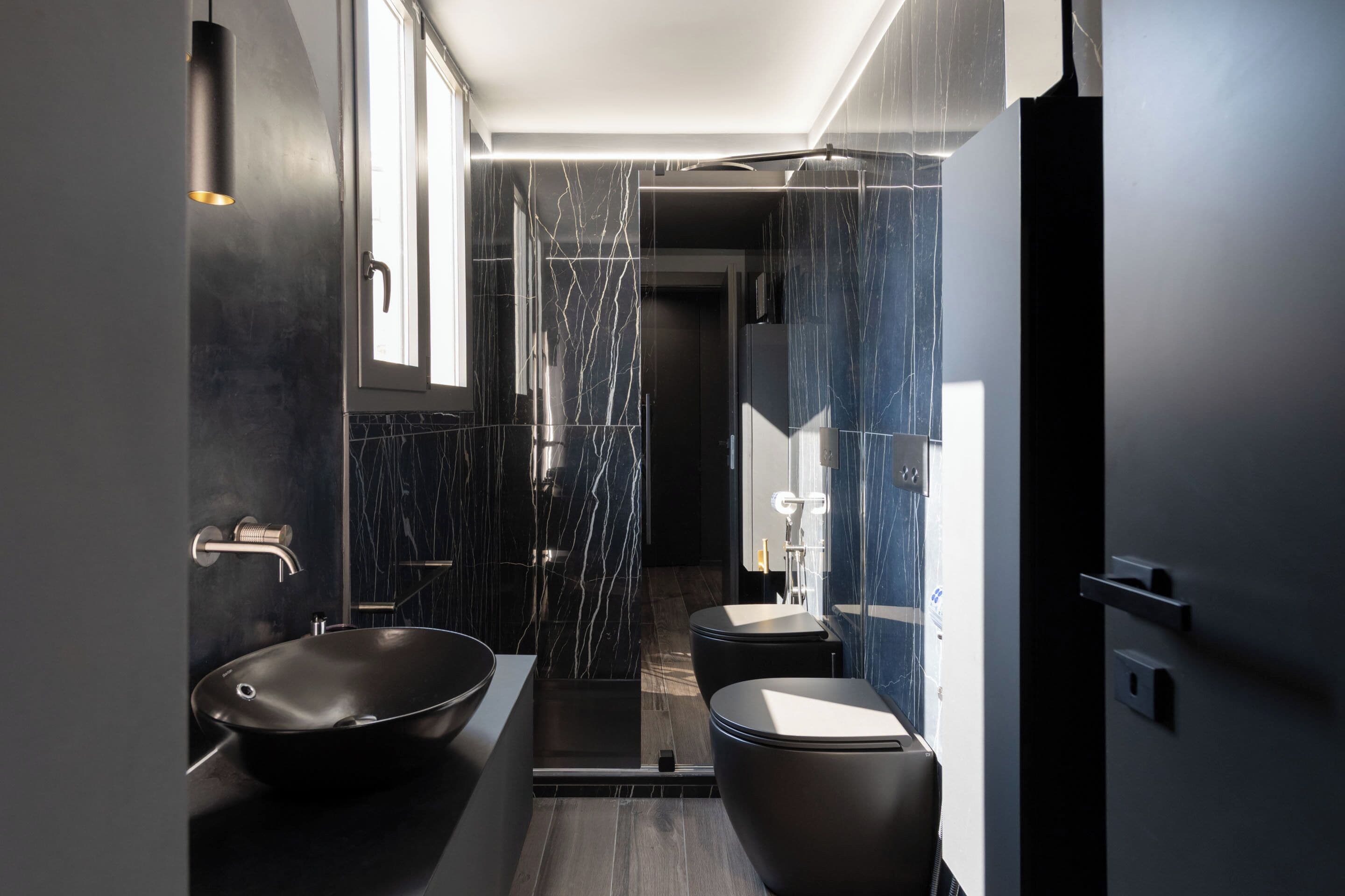 Un baño moderno con un lavabo de diseño negro, ducha a ras de suelo y un inodoro.