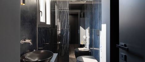 Un baño moderno con un lavabo de diseño negro, ducha a ras de suelo y un inodoro.