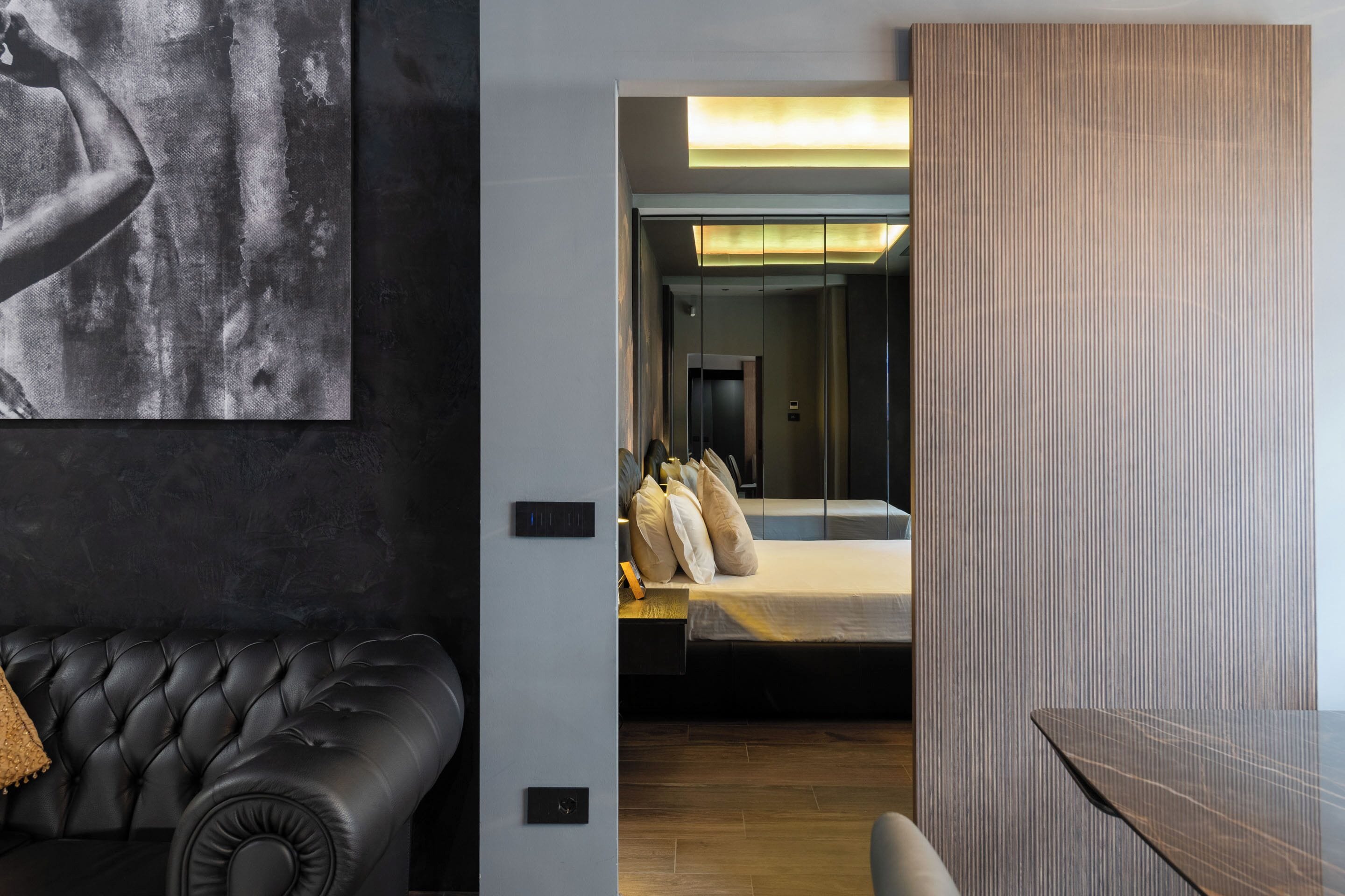Een moderne hotelkamer met een zwarte leren bank, een bed met houten hoofdbord, en een groot schilderij aan de muur.