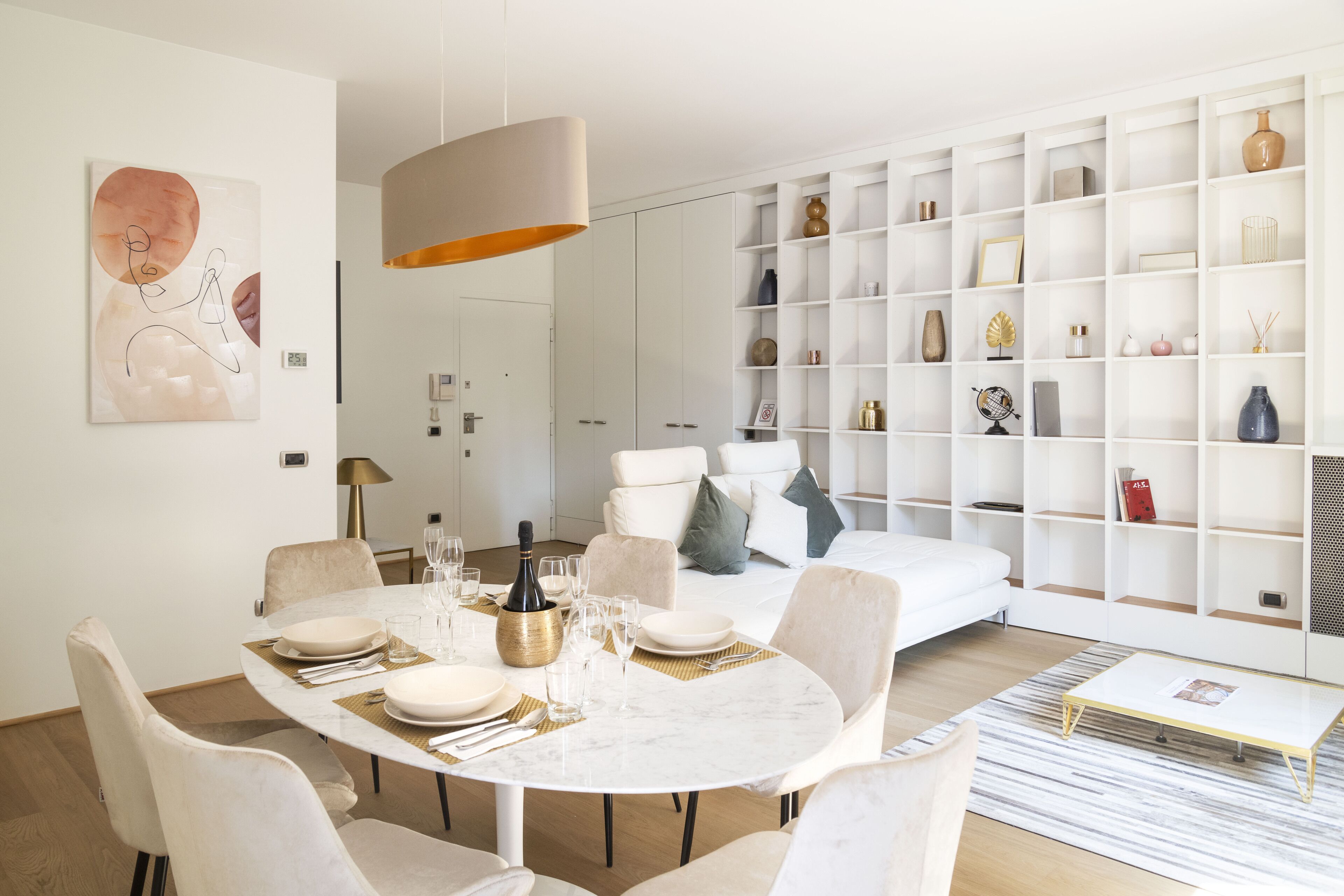 A modern living room with a dining area, white furniture, and a large bookshelf.