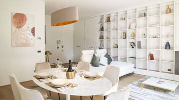 A modern living room with a dining area, white furniture, and a large bookshelf.