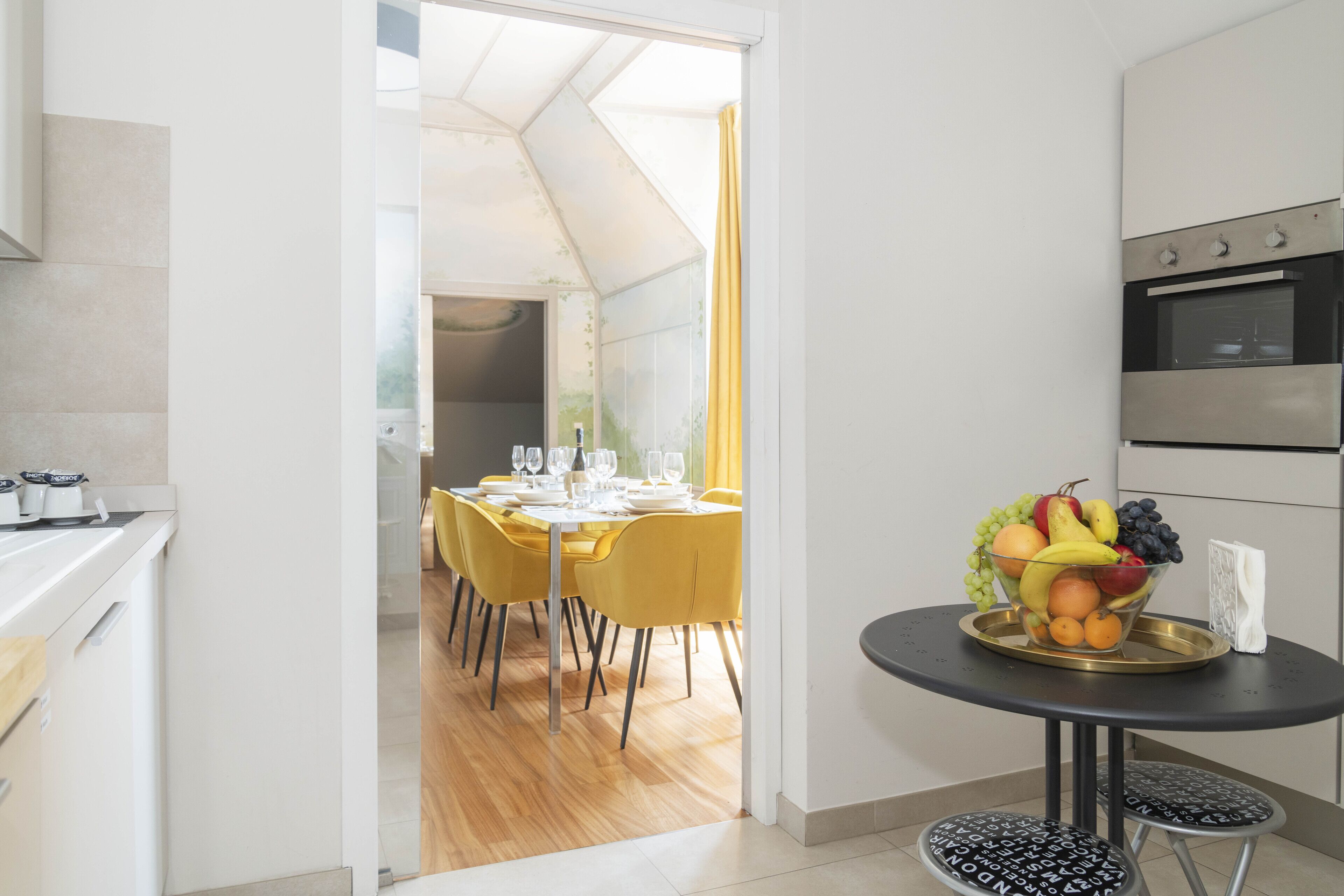 Une cuisine moderne avec un coin repas, un panier de fruits sur une table et une vue sur la salle à manger.