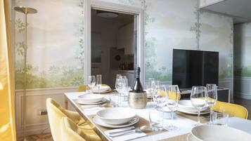 A dining room with a long table set for six, a TV in the background, and a kitchen visible through an open doorway.