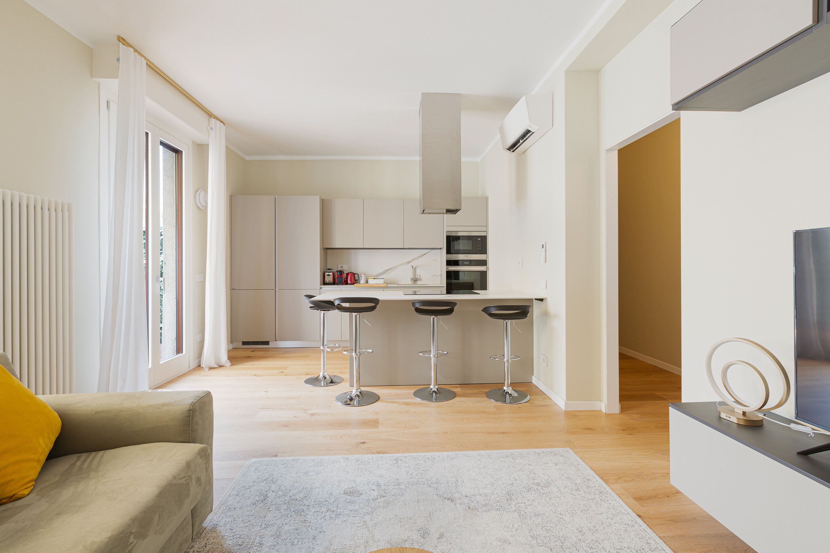 A modern kitchen with a central island, bar stools, and a TV on a stand.