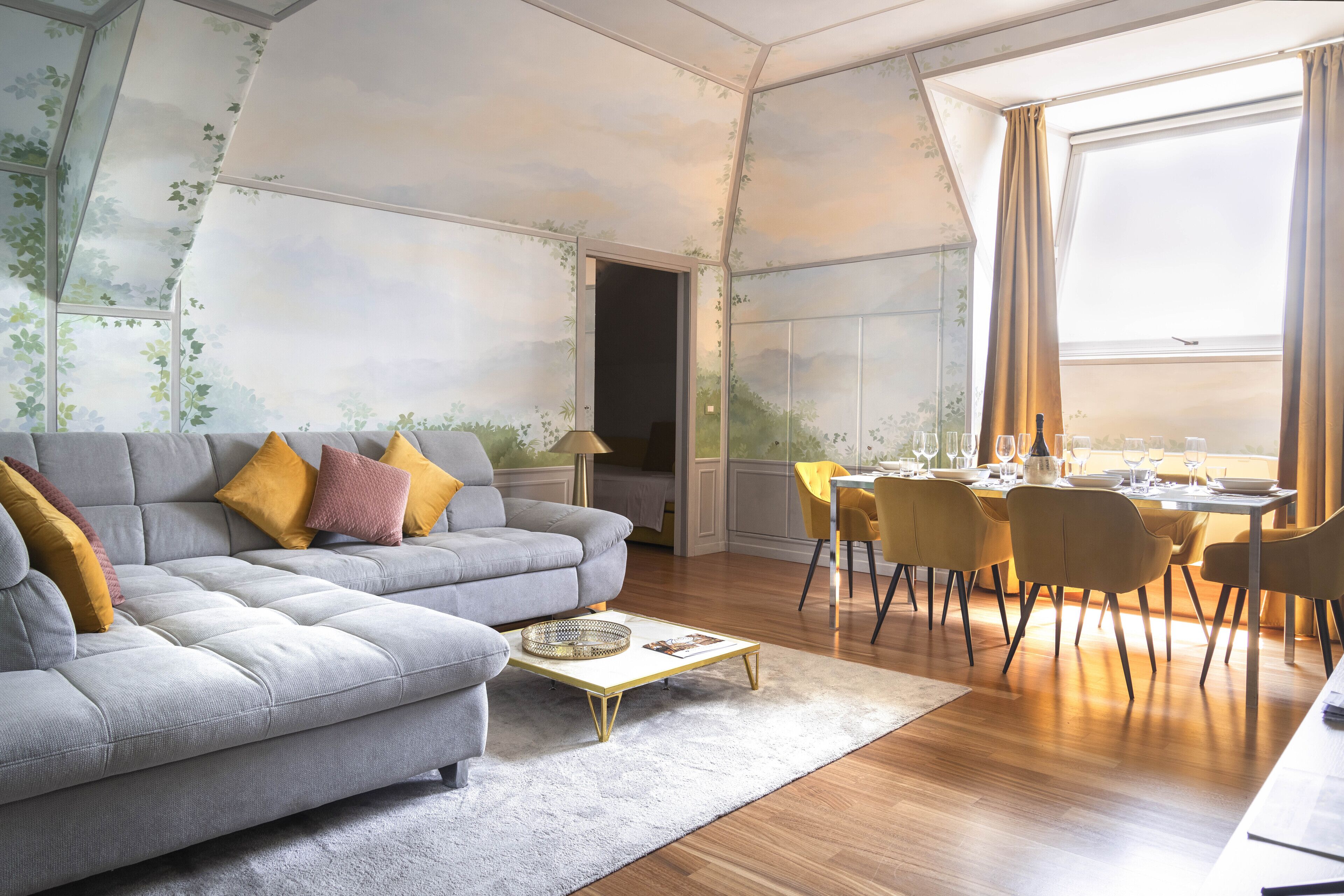 Ein modernes Wohnzimmer mit einem grauen Sofa, gelben Kissen, einem Couchtisch und einem Essbereich mit gelben Stühlen und einem für eine Mahlzeit gedeckten Tisch.