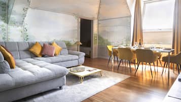 Ein modernes Wohnzimmer mit einem grauen Sofa, gelben Kissen, einem Couchtisch und einem Essbereich mit gelben Stühlen und einem für eine Mahlzeit gedeckten Tisch.