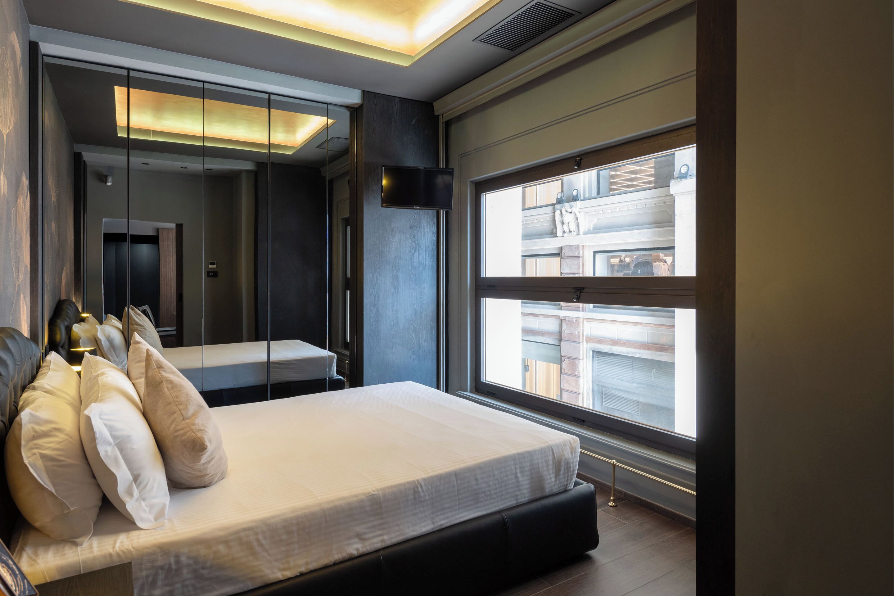 Un dormitorio moderno con una cama grande, un espejo y una ventana con vistas a un edificio.