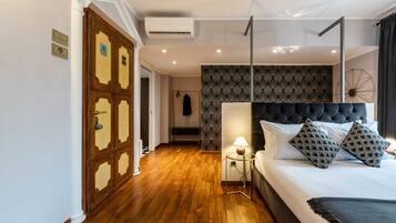 Een slaapkamer met een houten vloer, een bed met een zwart hoofdeinde, een nachtkastje met een lamp en een behang met een patroon.