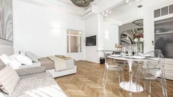 Un salon moderne avec un canapé, une table à manger et des chaises, et un coin cuisine visible à travers une porte ouverte.