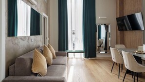 A modern living room with a sofa, a dining table with chairs, and a TV mounted on the wall.