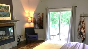 Een slaapkamer met een bed, een stoel, een open haard en een groot raam met uitzicht.