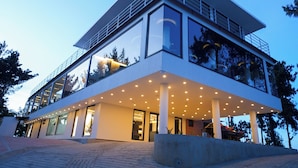 A modern multi-story building with large windows, a flat roof, and a covered outdoor area with seating.