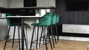 A modern kitchen with a bar area, featuring green bar stools, a microwave, and a flat-screen TV mounted on the wall.