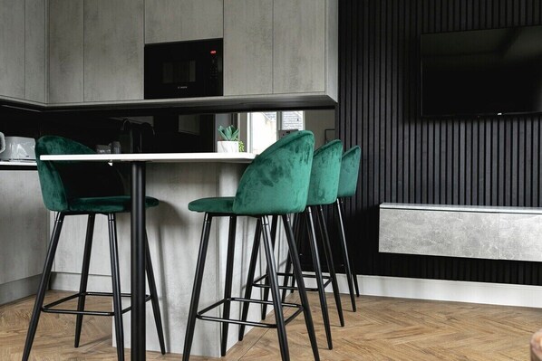 A modern kitchen with a bar area, featuring green bar stools, a microwave, and a flat-screen TV mounted on the wall. - Skyvillion Apartments-  Cockfosters - Spacious 1-Bed Apartment with Terrace (Barnet)