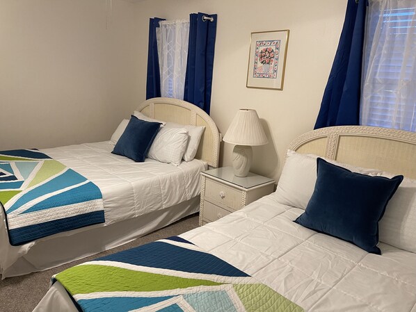 A double room with two beds, each with a white quilt and blue pillows, a bedside table with a lamp, and a framed picture on the wall. - Perfect Family Get Away! Amazing Prices! Pool! Complex is Beach Front! (Orange Beach)