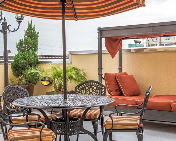An outdoor patio with a round metal table, cushioned chairs, a striped umbrella, and a sofa with red cushions.