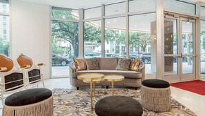 A modern lobby with a grey sofa, two round tables, wicker ottomans, and a patterned rug.
