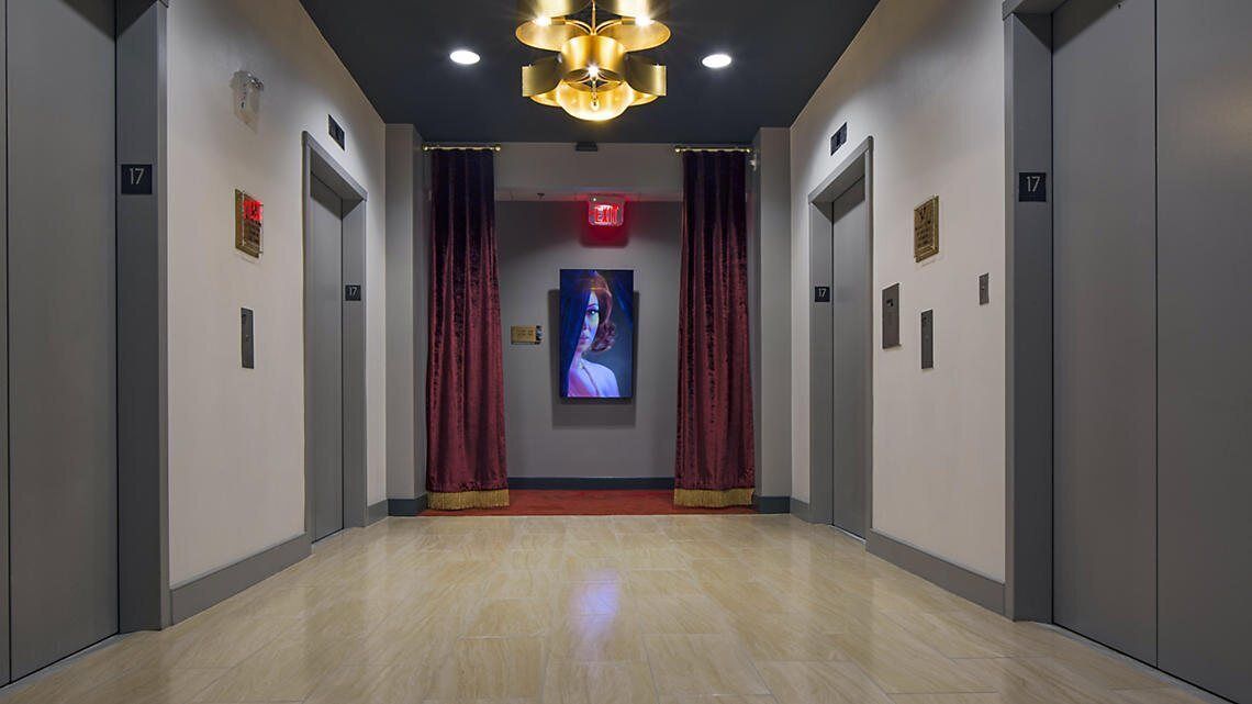 A modern elevator lobby with a marble floor, red curtains, and a central digital display.