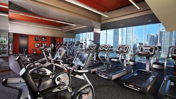 Un gimnasio moderno con cintas de correr, bicicletas estáticas y un amplio ventanal con vista a la ciudad.