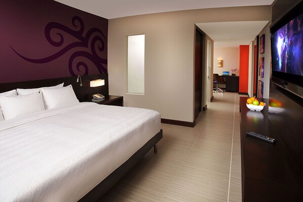 A hotel room with a large bed, a TV, a desk with a bowl of fruit, and a view of the hallway. - Megapolis Hotel Panamá (Panama City)