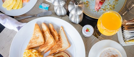 A breakfast setting with toast, scrambled eggs, bacon, pancakes, fruit, and coffee.