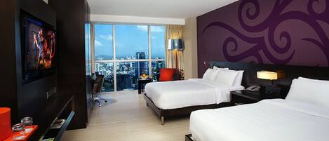 Habitación de hotel con dos camas, televisión, escritorio y un amplio ventanal con vista a la ciudad.