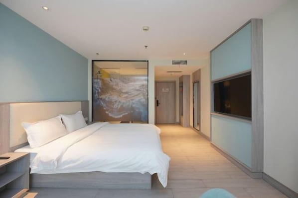 Habitación de hotel moderna con una cama grande, un televisor y vistas al pasillo.