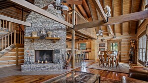 Amplia sala de estar con chimenea de piedra, vigas de madera y una mesa de centro de vidrio.